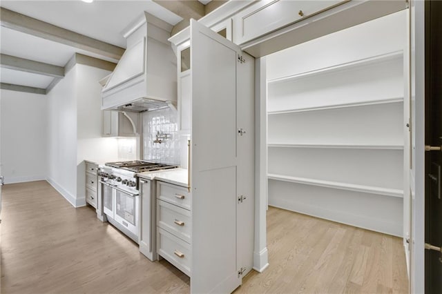 kitchen with white cabinetry, double oven range, custom exhaust hood, and light hardwood / wood-style floors