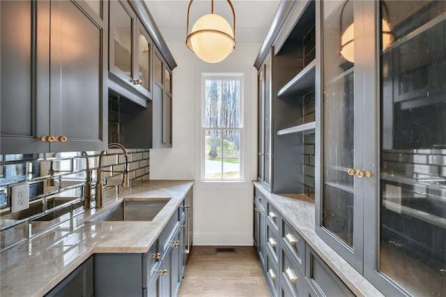 kitchen featuring decorative light fixtures, sink, decorative backsplash, light stone counters, and light wood-type flooring