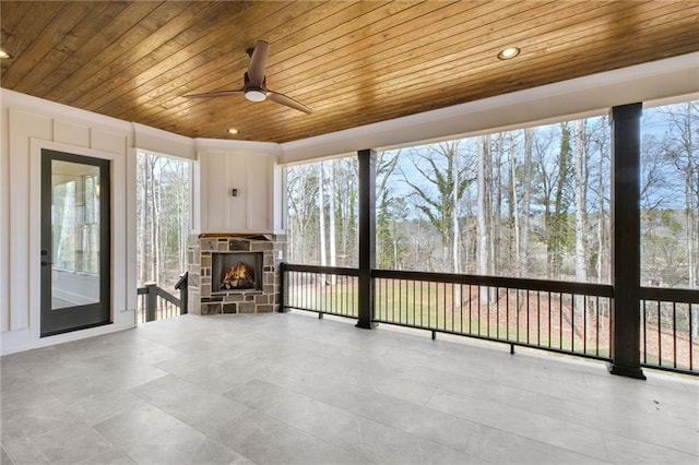 unfurnished sunroom featuring ceiling fan, wood ceiling, and an outdoor stone fireplace