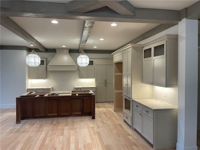 kitchen with beamed ceiling, custom range hood, light hardwood / wood-style floors, and decorative light fixtures