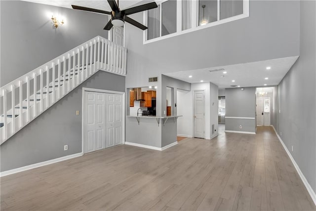 unfurnished living room with a ceiling fan, a towering ceiling, wood finished floors, baseboards, and stairs