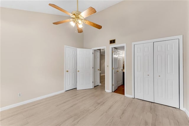 unfurnished bedroom with a high ceiling, baseboards, light wood-style flooring, a closet, and ceiling fan