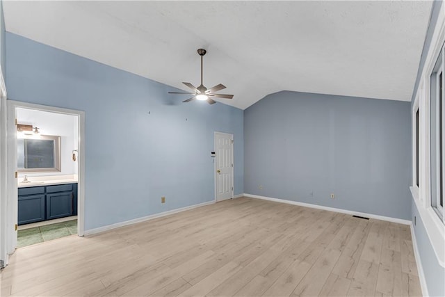 unfurnished bedroom featuring light wood finished floors, lofted ceiling, baseboards, connected bathroom, and a sink