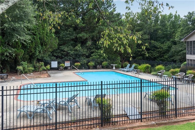 community pool featuring fence, a patio, and view of wooded area