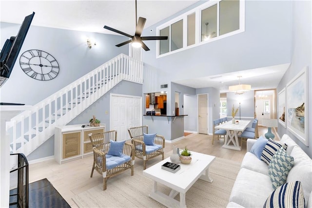 living room featuring a towering ceiling, stairs, a ceiling fan, baseboards, and wood finished floors
