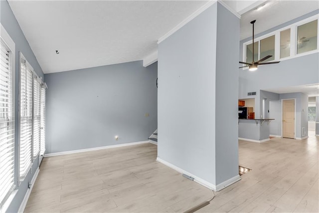 unfurnished living room with a ceiling fan, light wood finished floors, stairs, baseboards, and vaulted ceiling