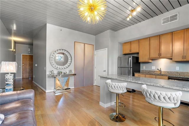 kitchen with light stone counters, a notable chandelier, stainless steel fridge, and a breakfast bar