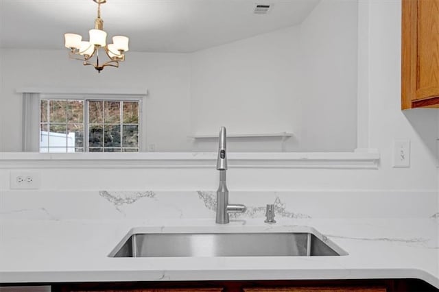 kitchen with visible vents, a notable chandelier, a sink, brown cabinetry, and hanging light fixtures