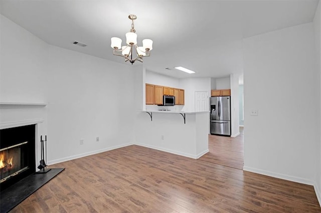 unfurnished living room featuring visible vents, a glass covered fireplace, wood finished floors, an inviting chandelier, and baseboards