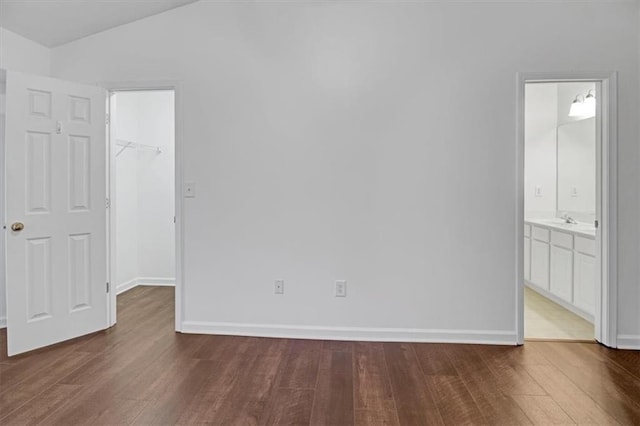 unfurnished bedroom with wood finished floors, a sink, vaulted ceiling, a closet, and a walk in closet