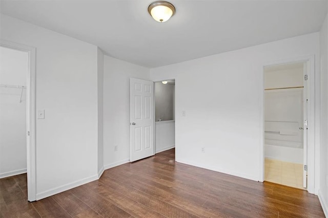 unfurnished bedroom with a closet, baseboards, dark wood-style flooring, and a spacious closet