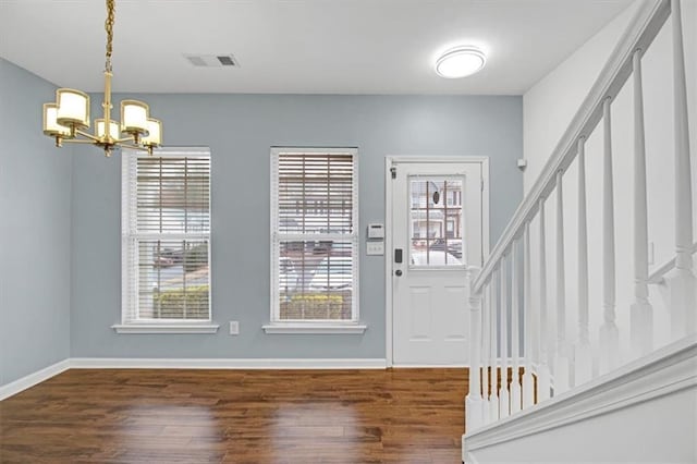 foyer featuring stairway, wood finished floors, a healthy amount of sunlight, and a chandelier