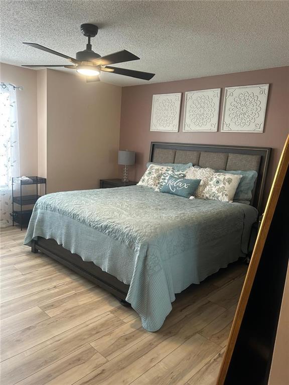 bedroom featuring ceiling fan, hardwood / wood-style floors, and a textured ceiling