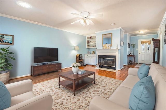 living room featuring baseboards, wood finished floors, a ceiling fan, and ornamental molding