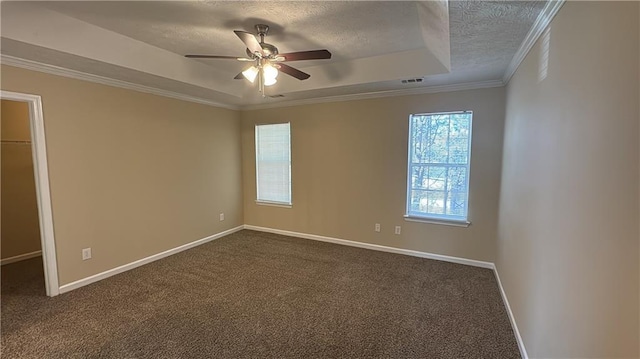 spare room with a textured ceiling, dark colored carpet, ornamental molding, and a raised ceiling