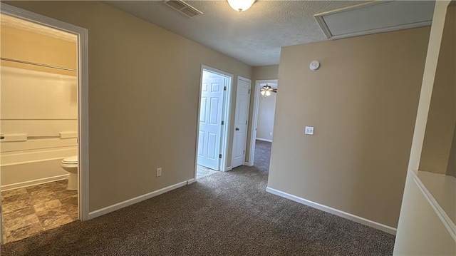 unfurnished bedroom featuring connected bathroom, a closet, a textured ceiling, and dark colored carpet