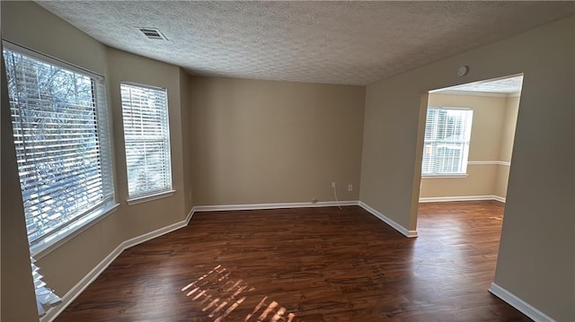 unfurnished room featuring a textured ceiling, a healthy amount of sunlight, and dark hardwood / wood-style floors