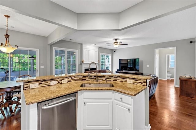 kitchen featuring stainless steel dishwasher, a kitchen island with sink, light stone countertops, open floor plan, and a sink