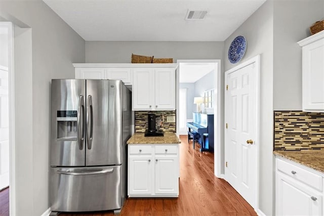 kitchen featuring dark wood finished floors, white cabinetry, decorative backsplash, stainless steel refrigerator with ice dispenser, and visible vents