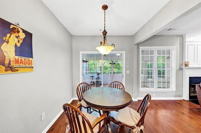 dining space featuring baseboards, wood finished floors, visible vents, and a large fireplace