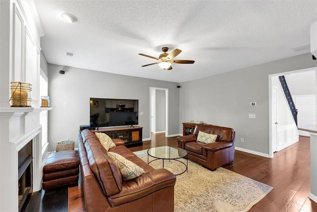 living room featuring visible vents, a fireplace, dark wood-type flooring, a textured ceiling, and a ceiling fan