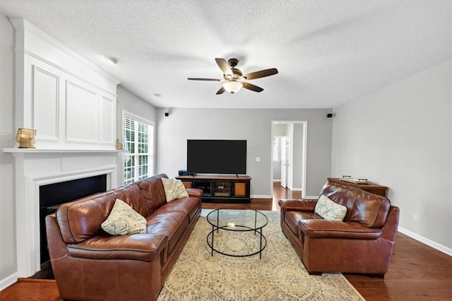 living area featuring ceiling fan, a textured ceiling, a fireplace, baseboards, and dark wood-style floors