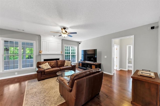 living room featuring a fireplace, a ceiling fan, a textured ceiling, and dark wood-type flooring