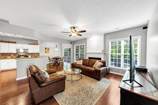 living area featuring a ceiling fan, a textured ceiling, dark wood-style floors, and a fireplace