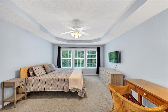 bedroom featuring a raised ceiling, ceiling fan, carpet, and a textured ceiling