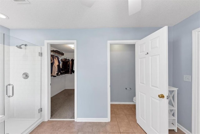 full bathroom with tile patterned flooring, a textured ceiling, a spacious closet, and a shower stall