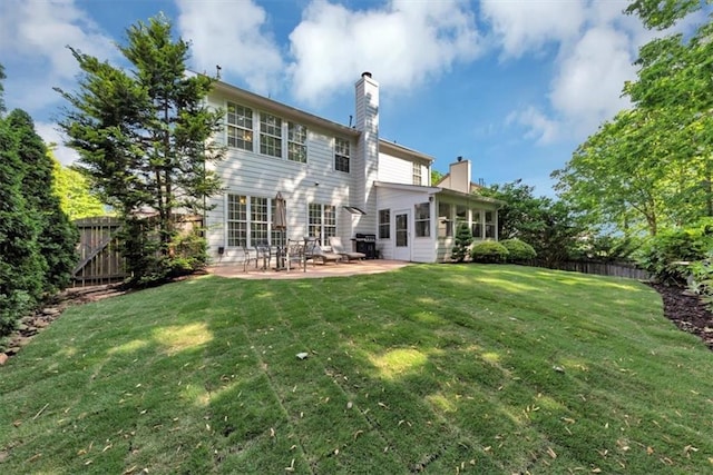 back of property with a sunroom, a chimney, a lawn, a patio, and fence private yard