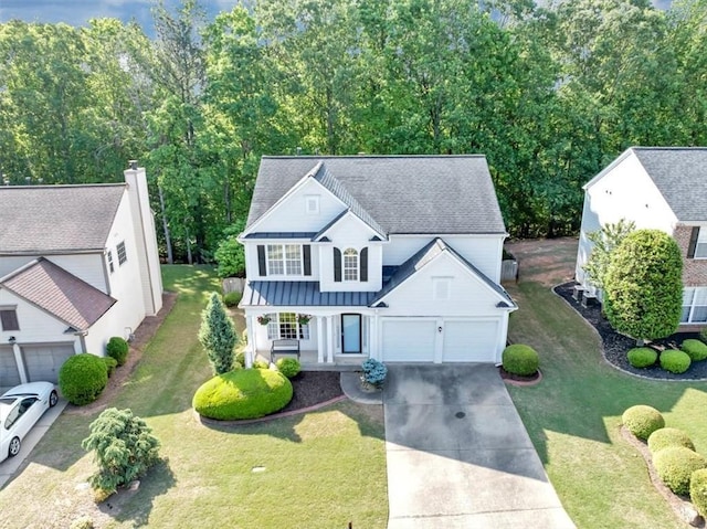 view of front of property with a front yard, a standing seam roof, a shingled roof, concrete driveway, and a porch