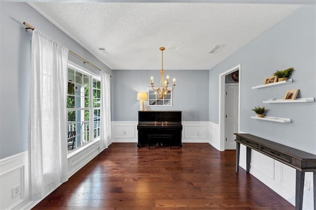 dining space with a textured ceiling, visible vents, wainscoting, wood finished floors, and a notable chandelier