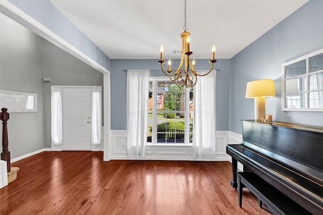 entrance foyer featuring a textured ceiling, a notable chandelier, a healthy amount of sunlight, and wood finished floors
