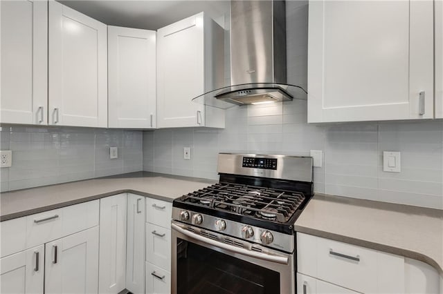 kitchen featuring wall chimney range hood, stainless steel gas range oven, white cabinetry, and decorative backsplash
