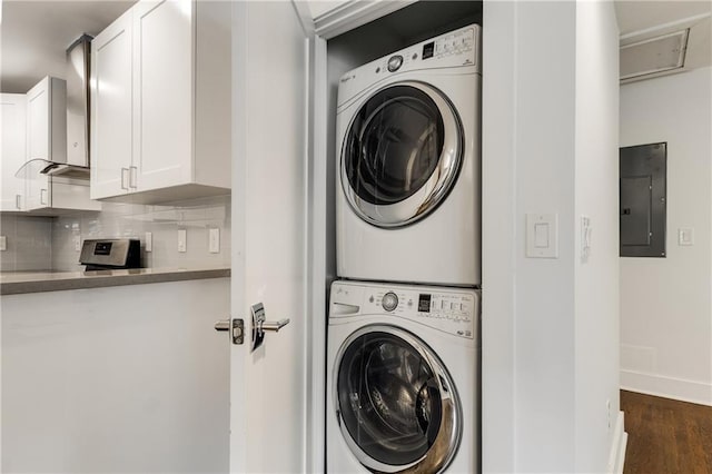 laundry room with stacked washer / dryer, electric panel, dark wood-style floors, baseboards, and attic access
