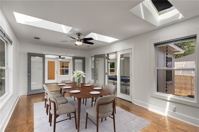 dining room featuring a skylight, baseboards, wood finished floors, and ceiling fan
