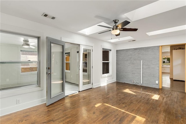 empty room with a skylight, wood finished floors, a ceiling fan, and baseboards