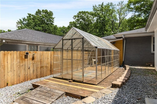 wooden terrace with a greenhouse, an outbuilding, and fence
