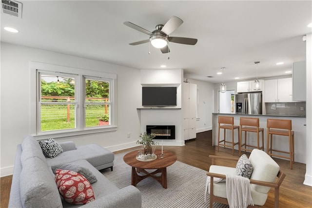 living area with recessed lighting, dark wood finished floors, a ceiling fan, a glass covered fireplace, and baseboards