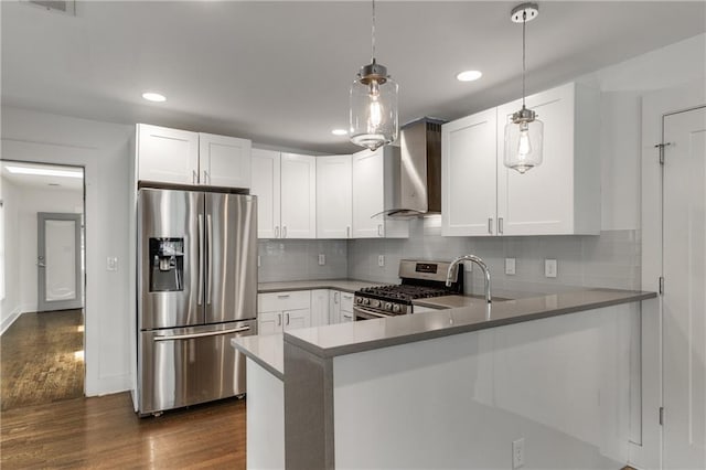 kitchen featuring appliances with stainless steel finishes, wall chimney range hood, a sink, dark wood-style flooring, and a peninsula