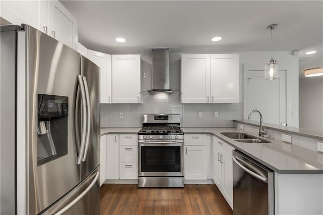 kitchen featuring appliances with stainless steel finishes, wall chimney range hood, a sink, a peninsula, and dark wood-style floors