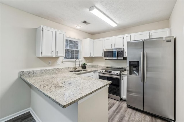 kitchen featuring appliances with stainless steel finishes, a textured ceiling, white cabinetry, sink, and kitchen peninsula