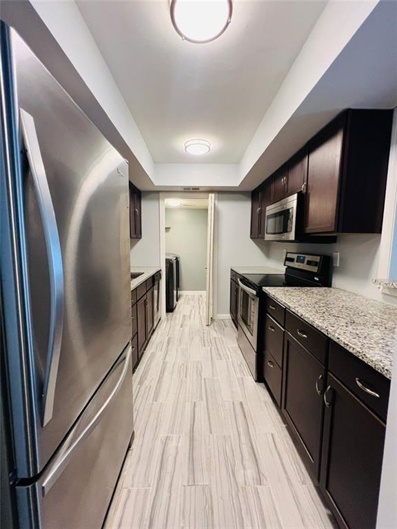 3432 Ivys Walk, Atlanta, GA 30340 - kitchen with stainless steel appliances, washer and dryer, dark brown cabinets, and baseboards