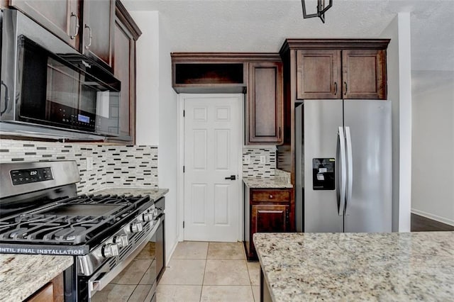 kitchen featuring light tile patterned floors, stainless steel appliances, tasteful backsplash, light stone countertops, and a textured ceiling