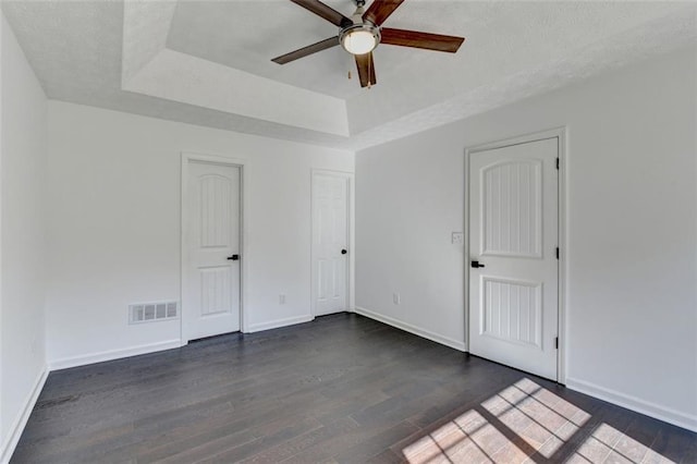 unfurnished room with ceiling fan, a tray ceiling, dark hardwood / wood-style flooring, and a textured ceiling