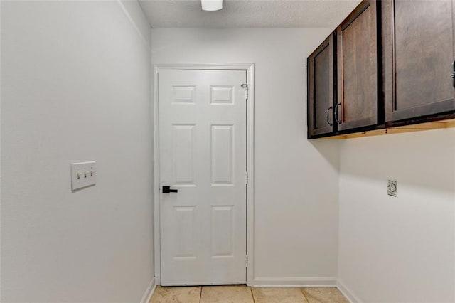 clothes washing area with cabinets, a textured ceiling, and light tile patterned flooring