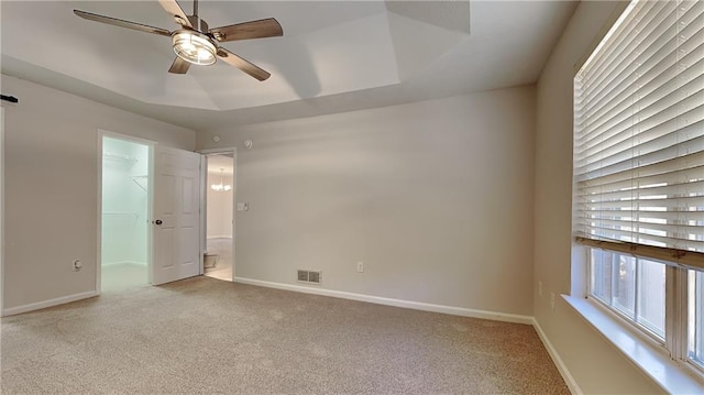 unfurnished room featuring a raised ceiling, light carpet, and ceiling fan