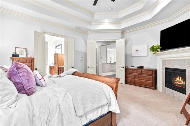 carpeted bedroom featuring connected bathroom, ceiling fan, a tray ceiling, a fireplace, and ornamental molding