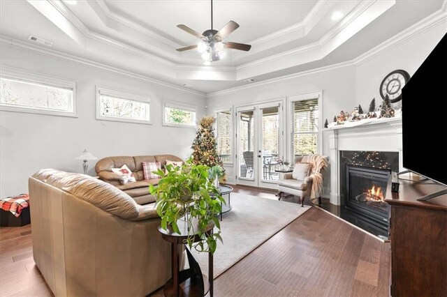 living room with a raised ceiling, a tile fireplace, crown molding, and hardwood / wood-style floors